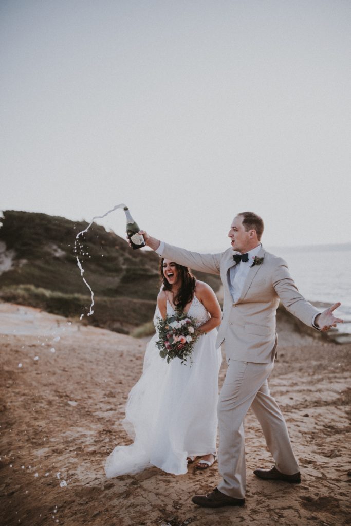 a couple popping a bottle of champagne after their elopement at cape kiwanda